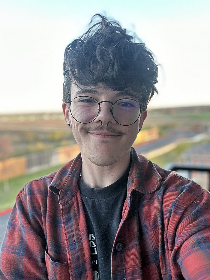 Wyatt Denham smiling in a red plaid shirt and black glasses